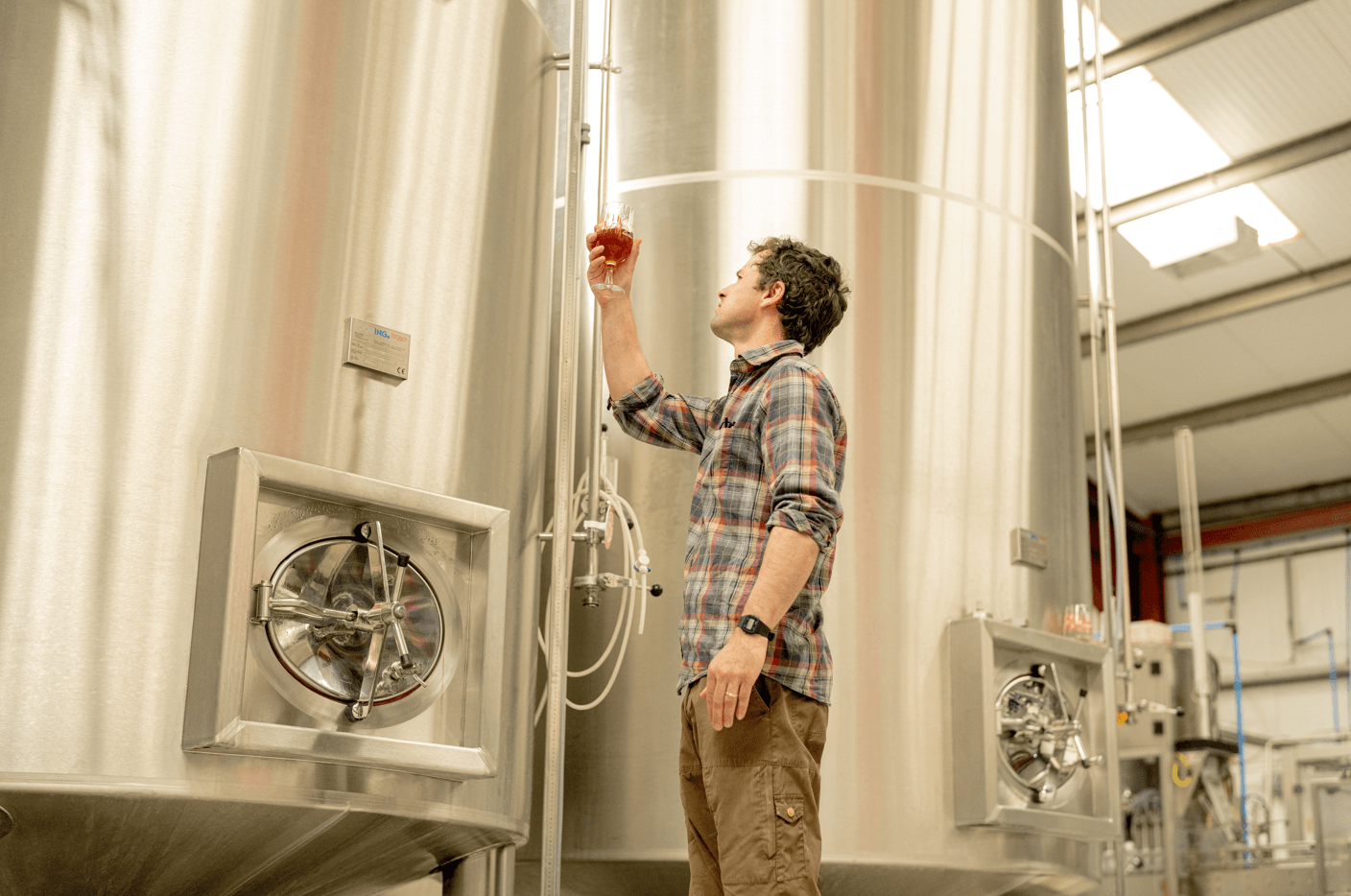 person standing in a brewery inspecting a glass of beer